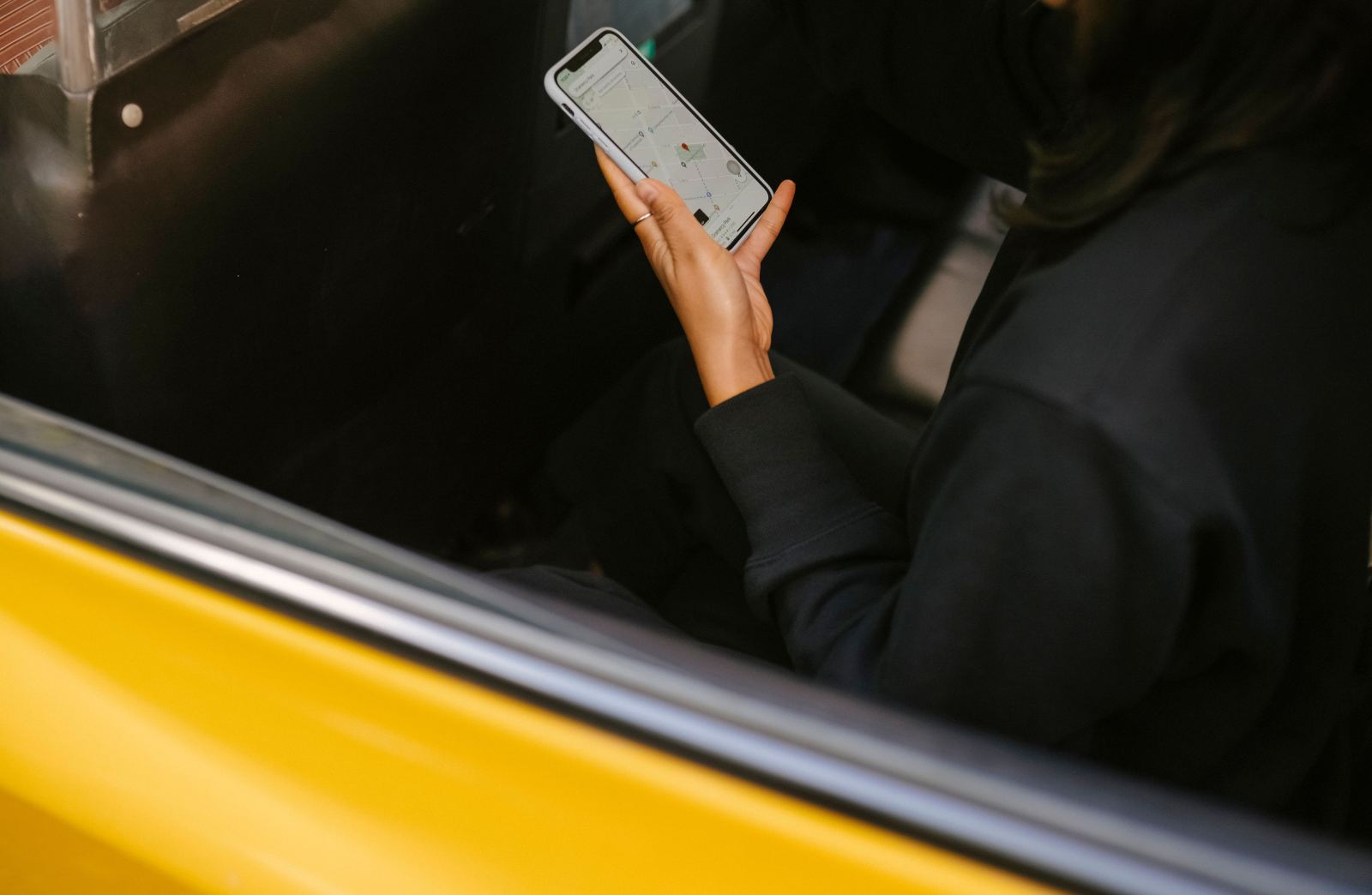Passenger holding a phone with a map app open inside a yellow taxi