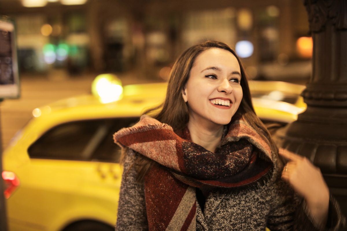 Woman standing near a yellow taxi on a city street at night