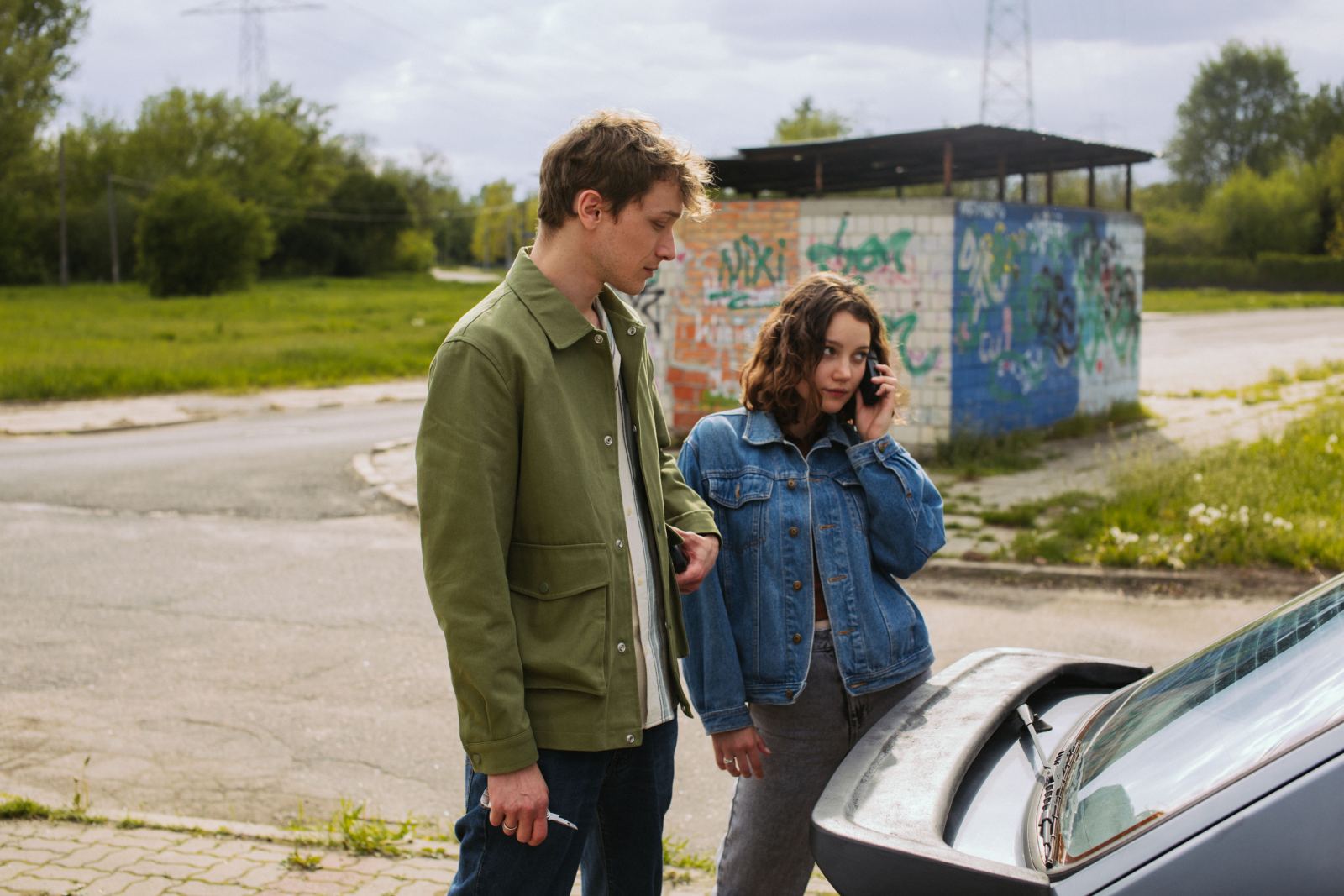 Couple standing beside a car with the trunk open, one on the phone