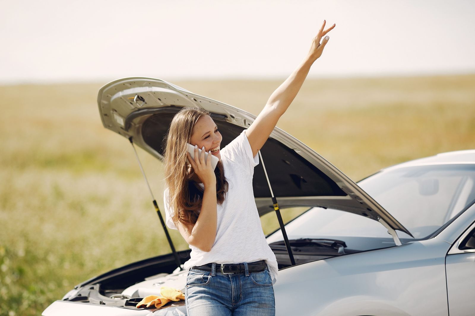 Woman celebrating on the phone next to her car with the hood open after roadside help arrives