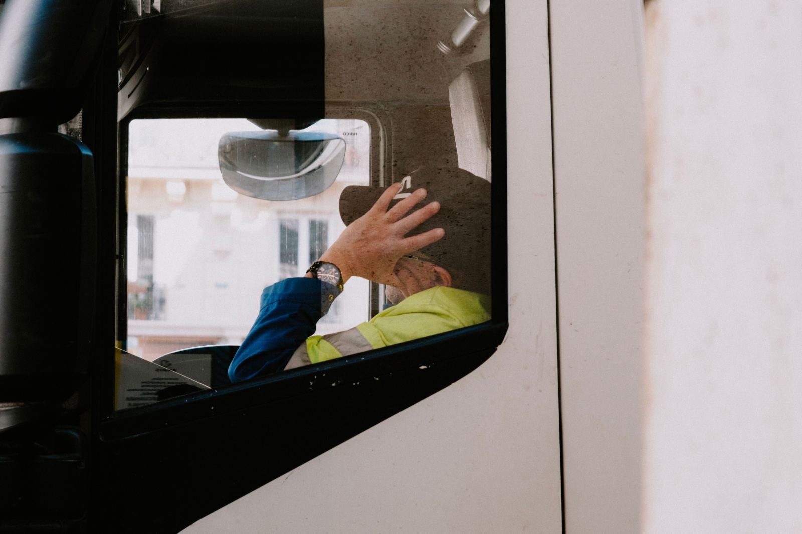 Truck driver in a high-visibility jacket seen through the cab window