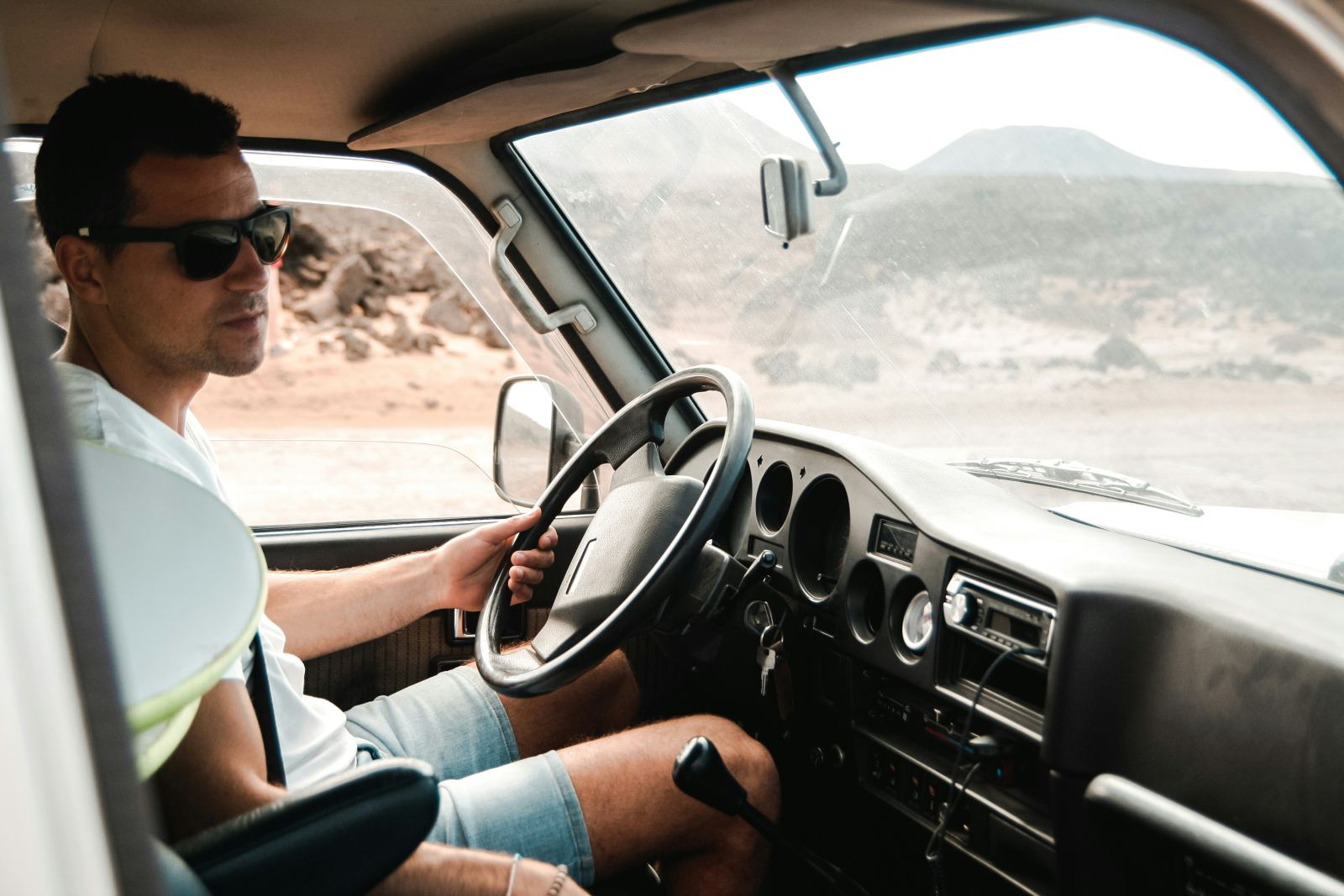 Driver wearing sunglasses behind the wheel of a vehicle in a rocky landscape