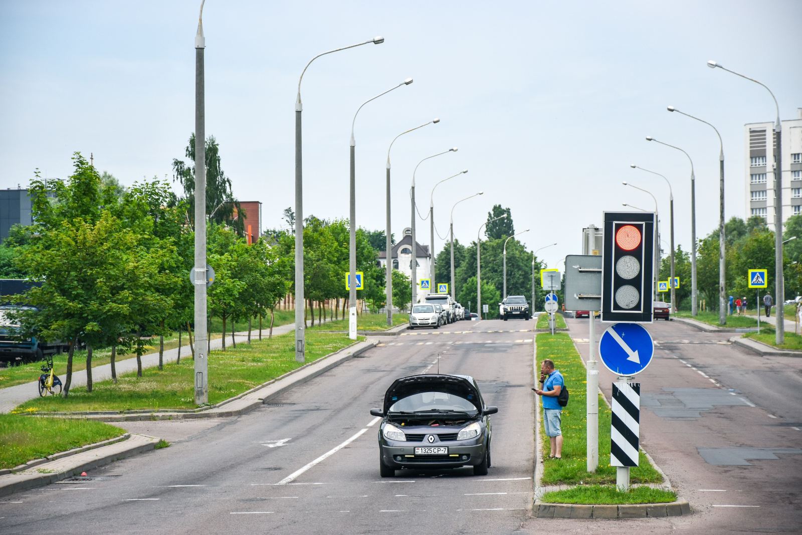 Man on the phone beside a car with its hood open on a city street