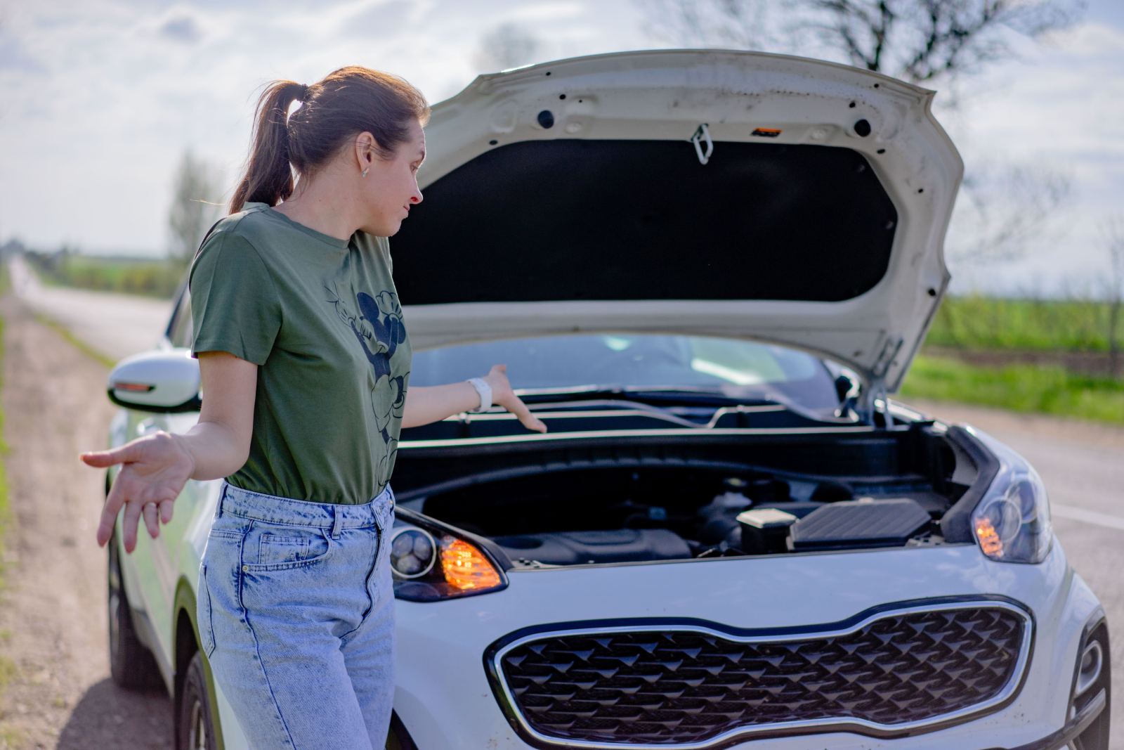 Woman looking puzzled beside her car with the hood open