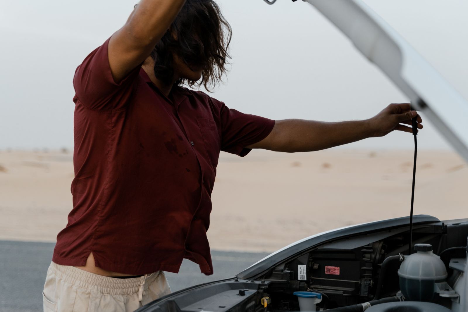 Man checking under the hood of a car on a desert road
