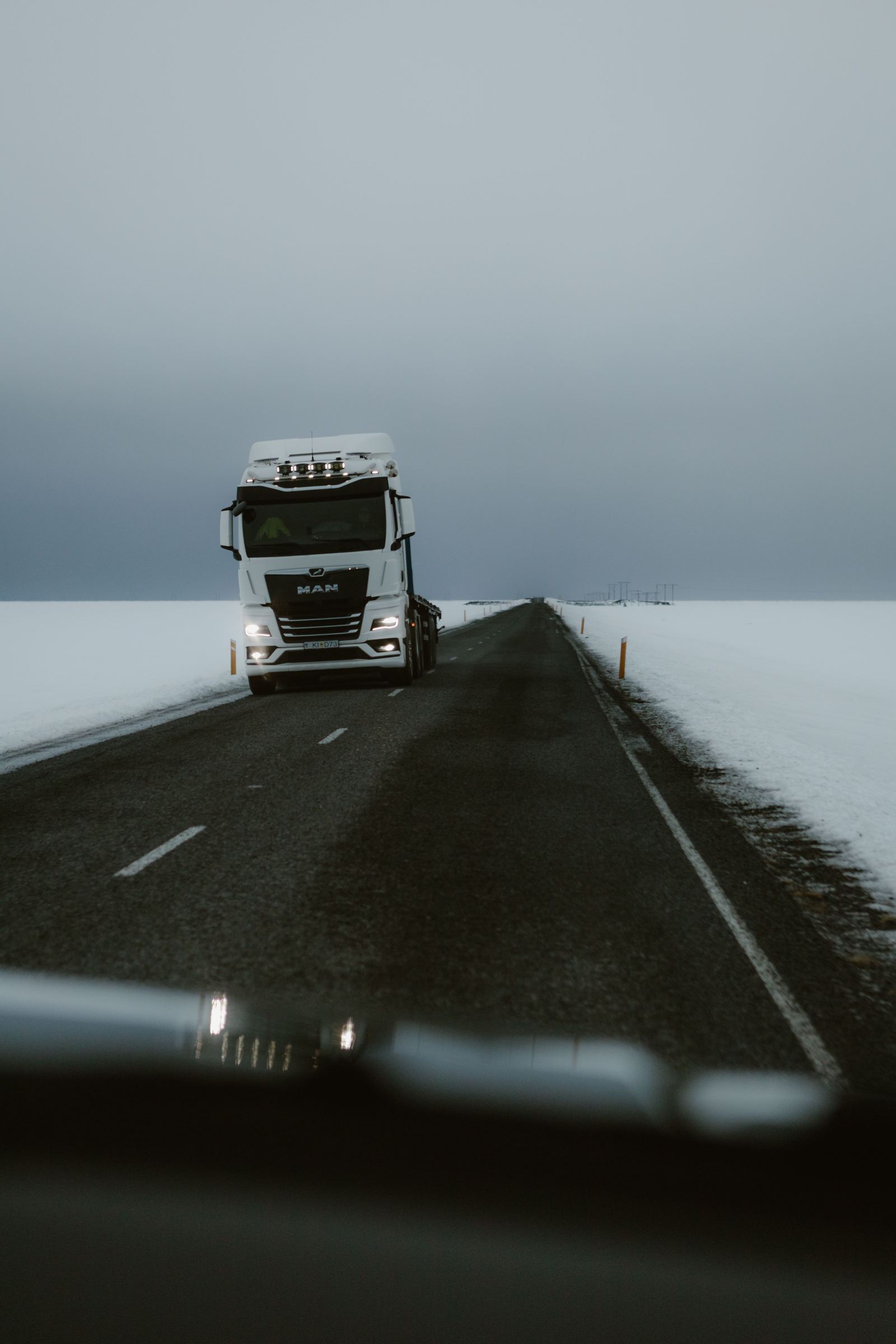 Heavy truck driving down a snow-covered road at dusk