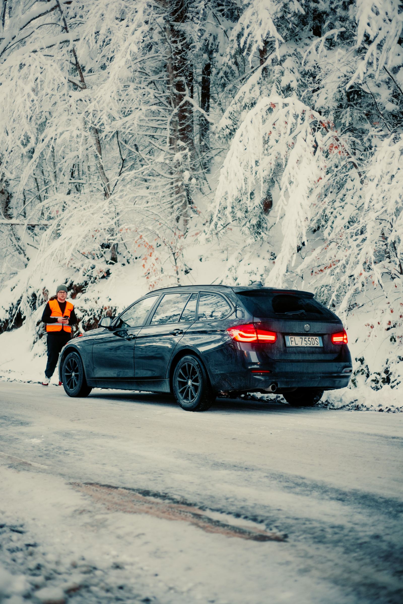 Roadside assistance worker in a safety vest beside a car stopped on a snowy road