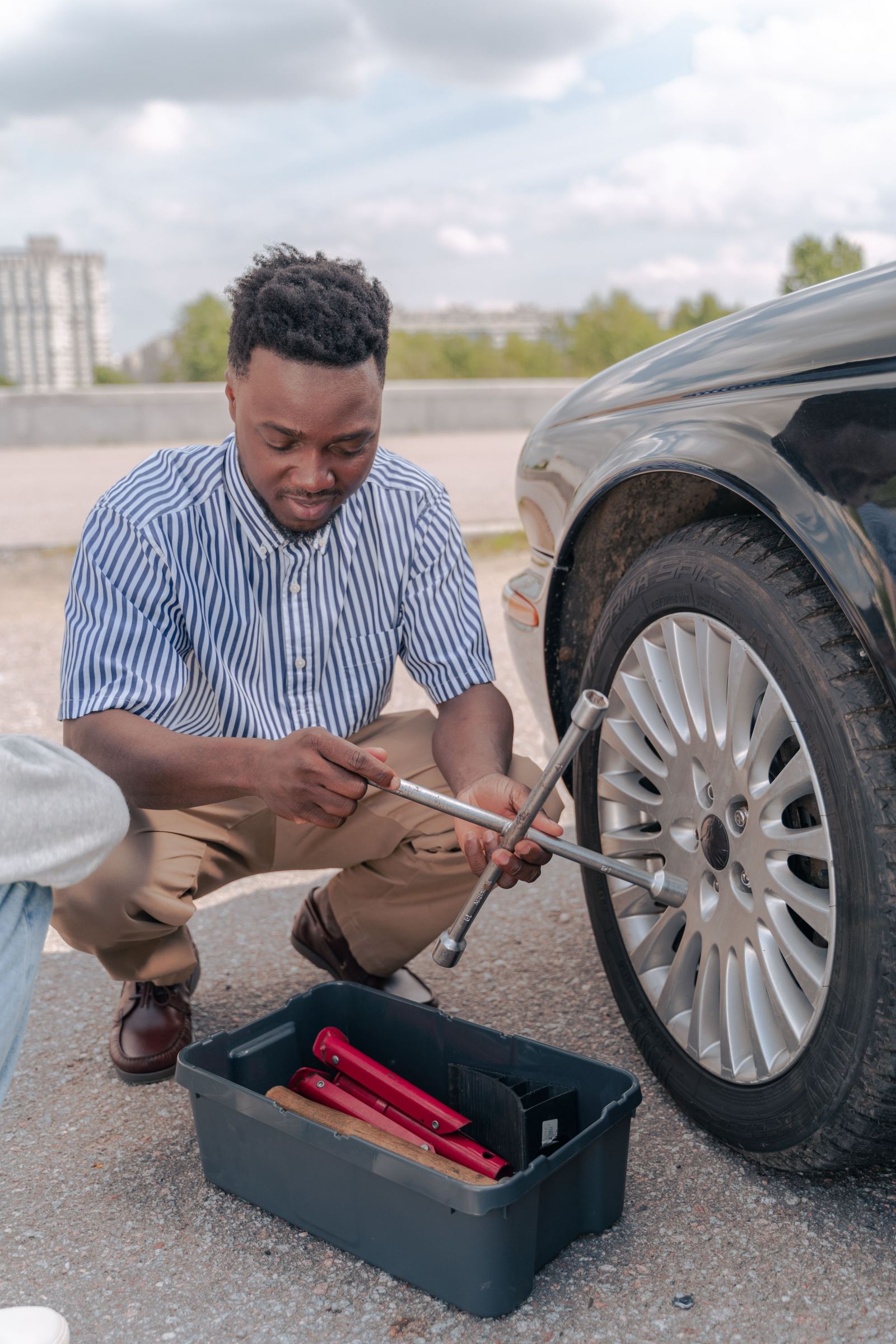 Man kneeling to change a car tire on the roadside with a lug wrench