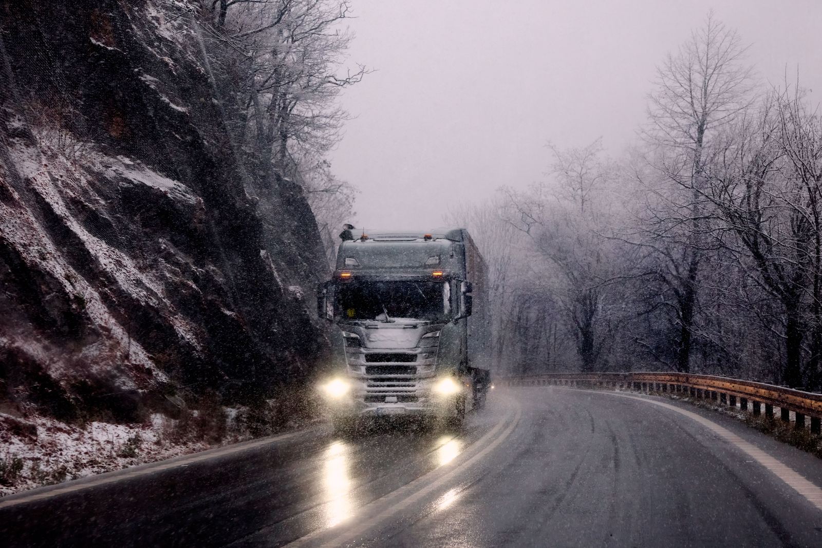 Heavy truck driving through a snowy mountain road in foggy conditions