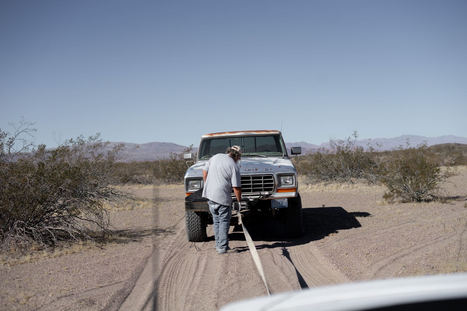 Man operating a winch to recover a truck on a desert trail