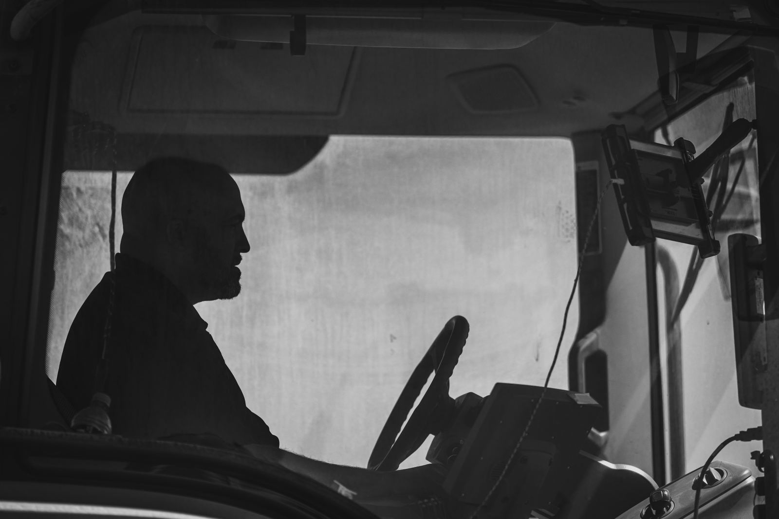 Black-and-white silhouette of a truck driver seated behind the wheel