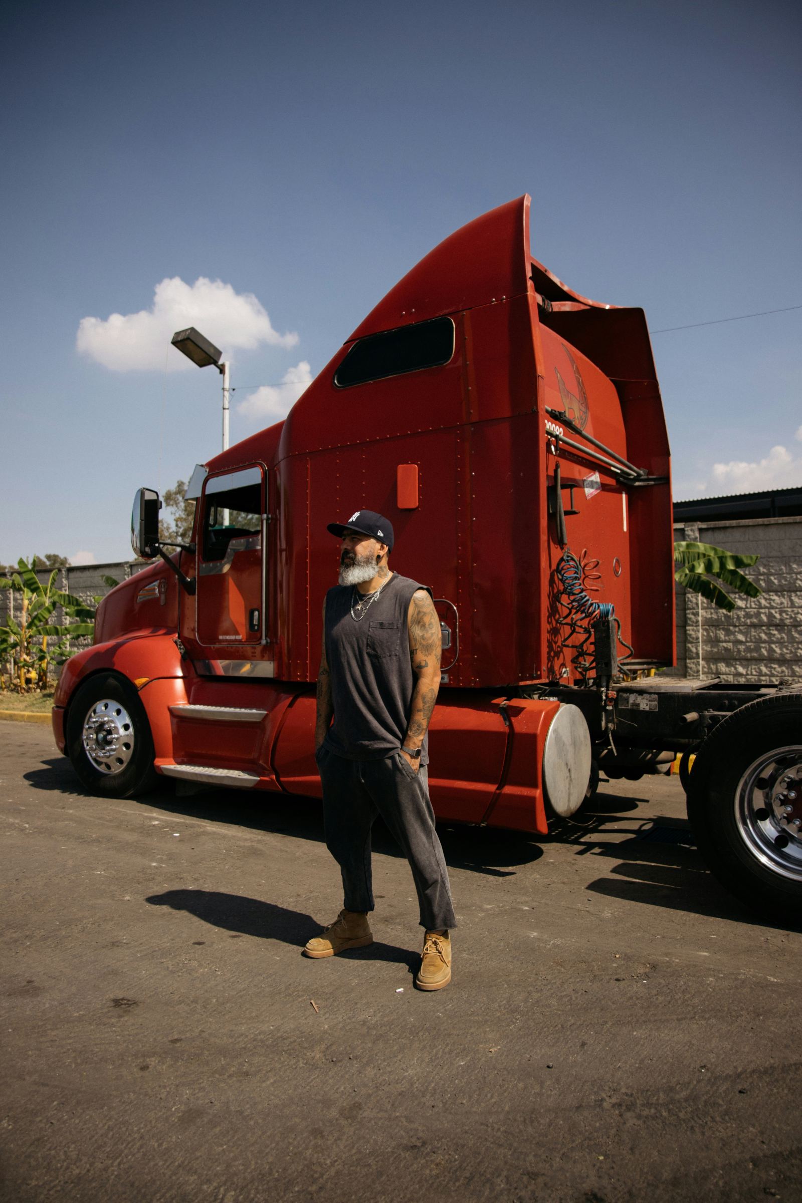 Tattooed owner-operator standing in front of his red semi truck