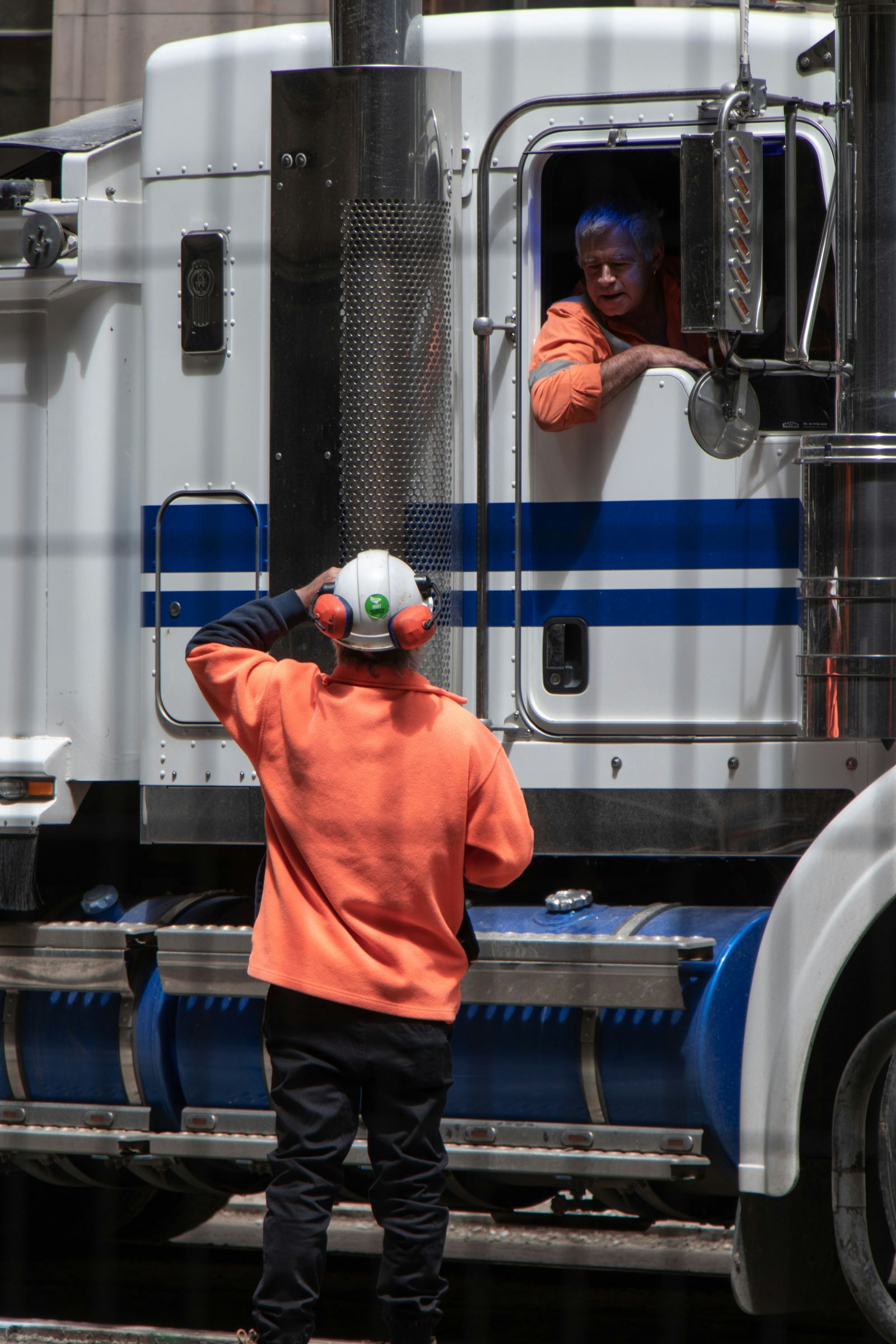 Worker in safety gear greeting a truck driver leaning out the cab window