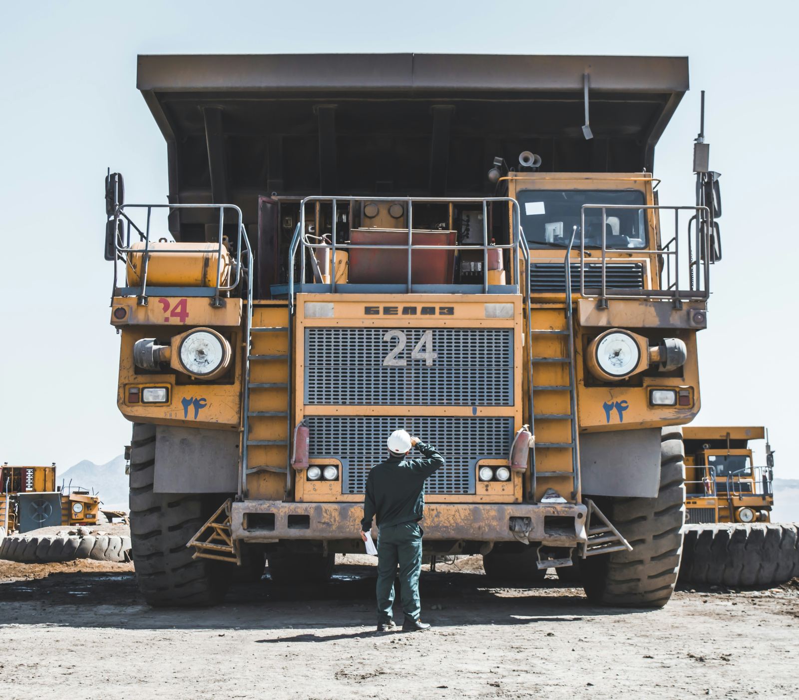Worker in a hard hat standing before a massive mining dump truck