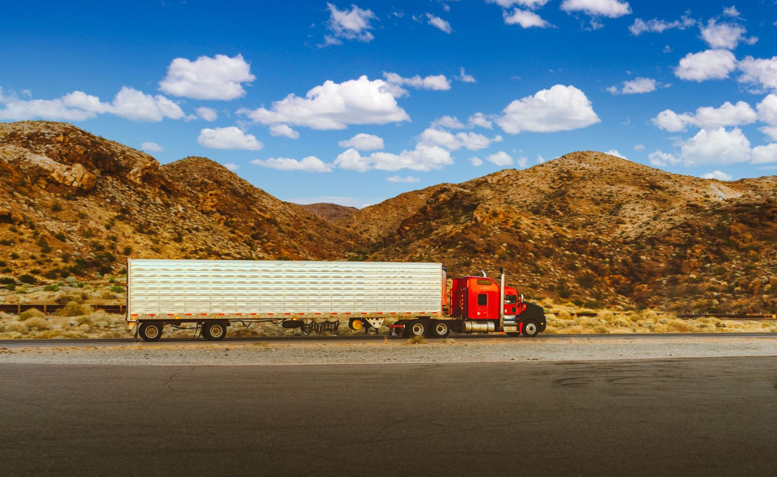 Red semi truck with a refrigerated trailer driving through a desert landscape