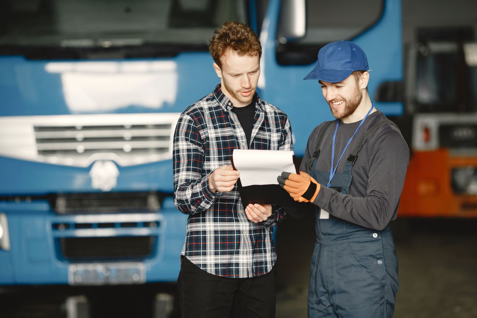 Two men reviewing a clipboard together in front of a truck in a garage