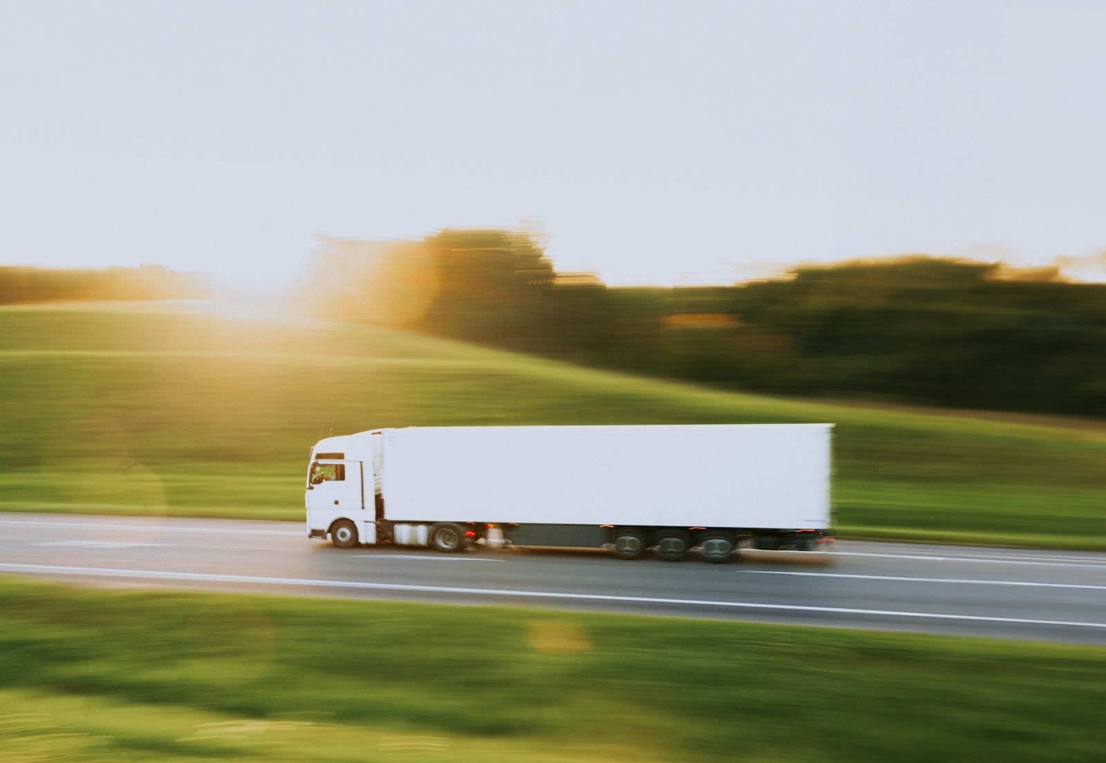 White semi truck driving at speed on a highway with motion-blurred scenery