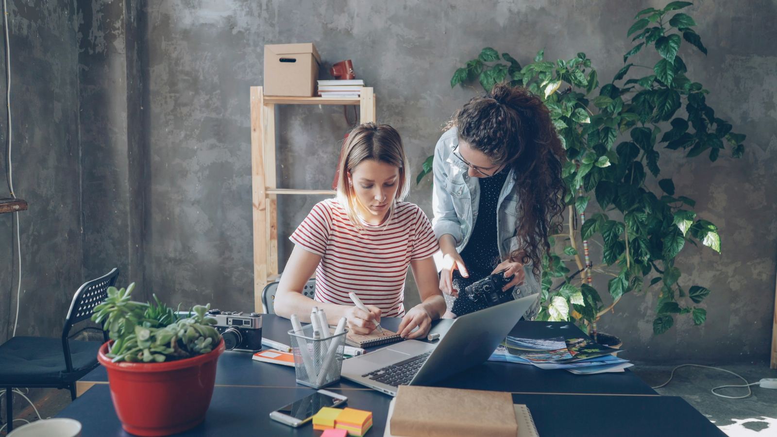 Two colleagues collaborating at a desk with a camera and laptop