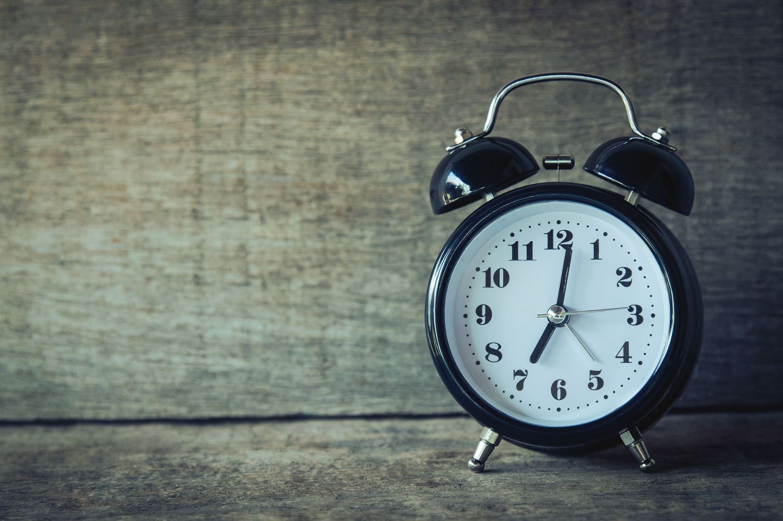 Vintage black alarm clock standing on a wooden surface