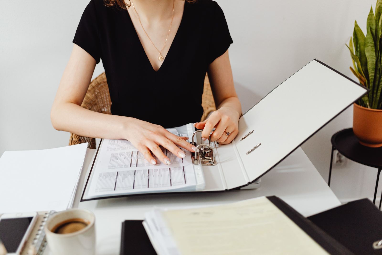 Woman opening a binder of printed spreadsheets at an office desk