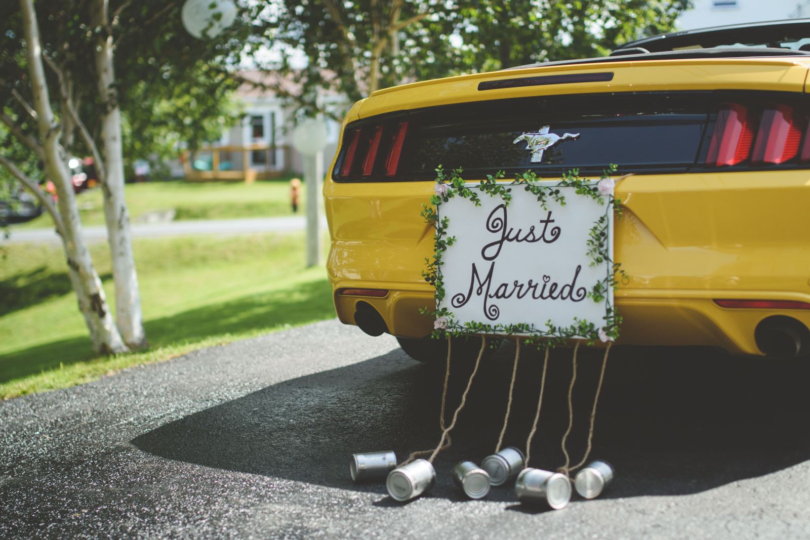 Yellow car with a Just Married sign and tin cans tied to the rear bumper