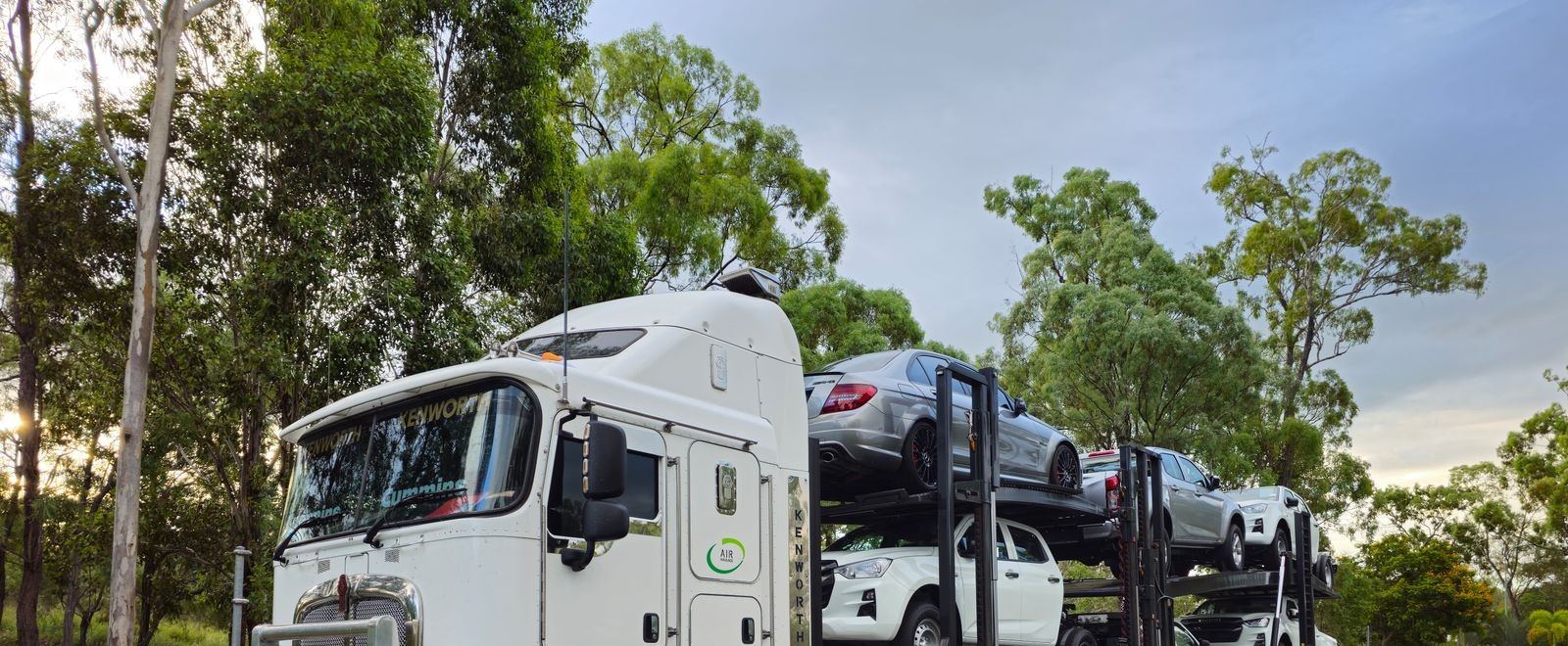 Car hauler truck loaded with multiple vehicles on a tree-lined road