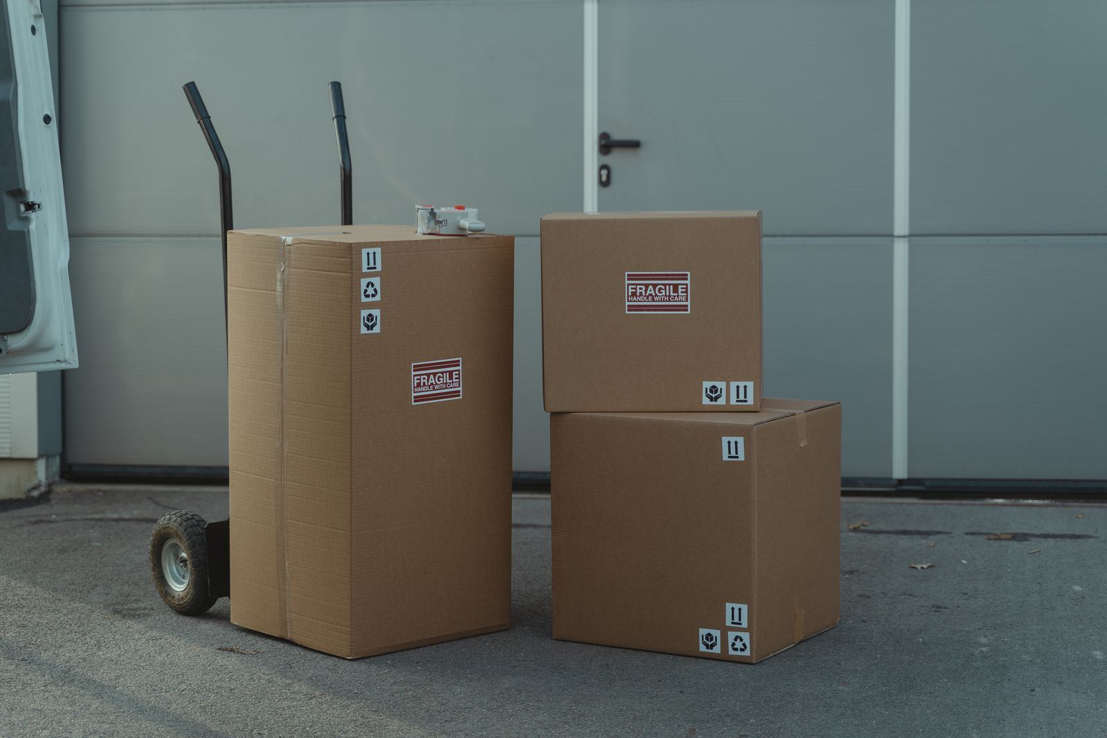 Stacked moving boxes marked fragile beside a hand truck outside a van