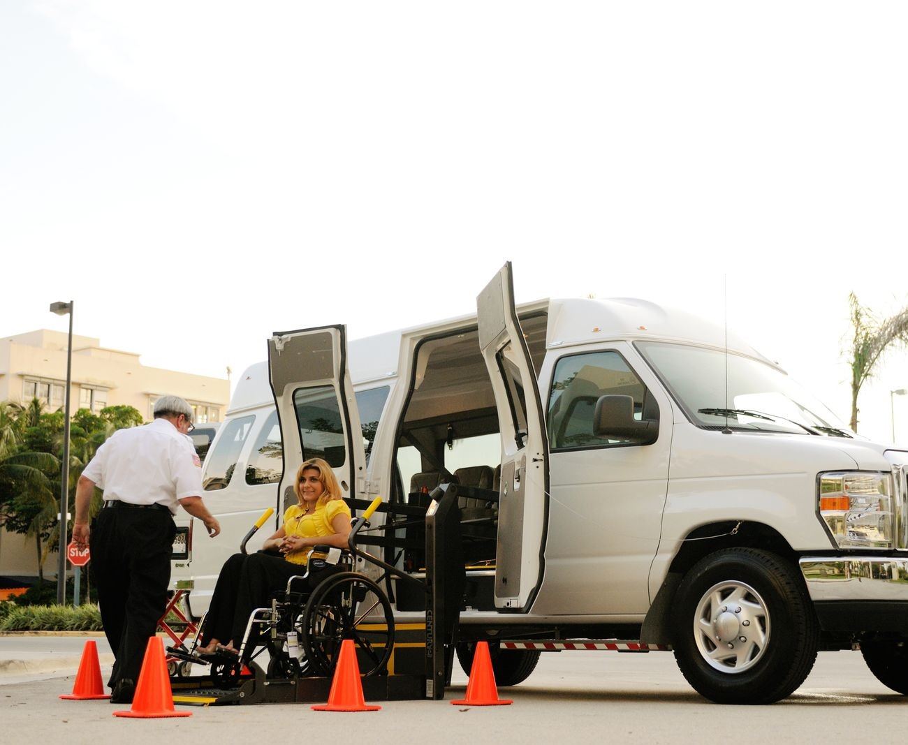 Wheelchair user boarding an accessible medical transport van via a lift, assisted by a driver