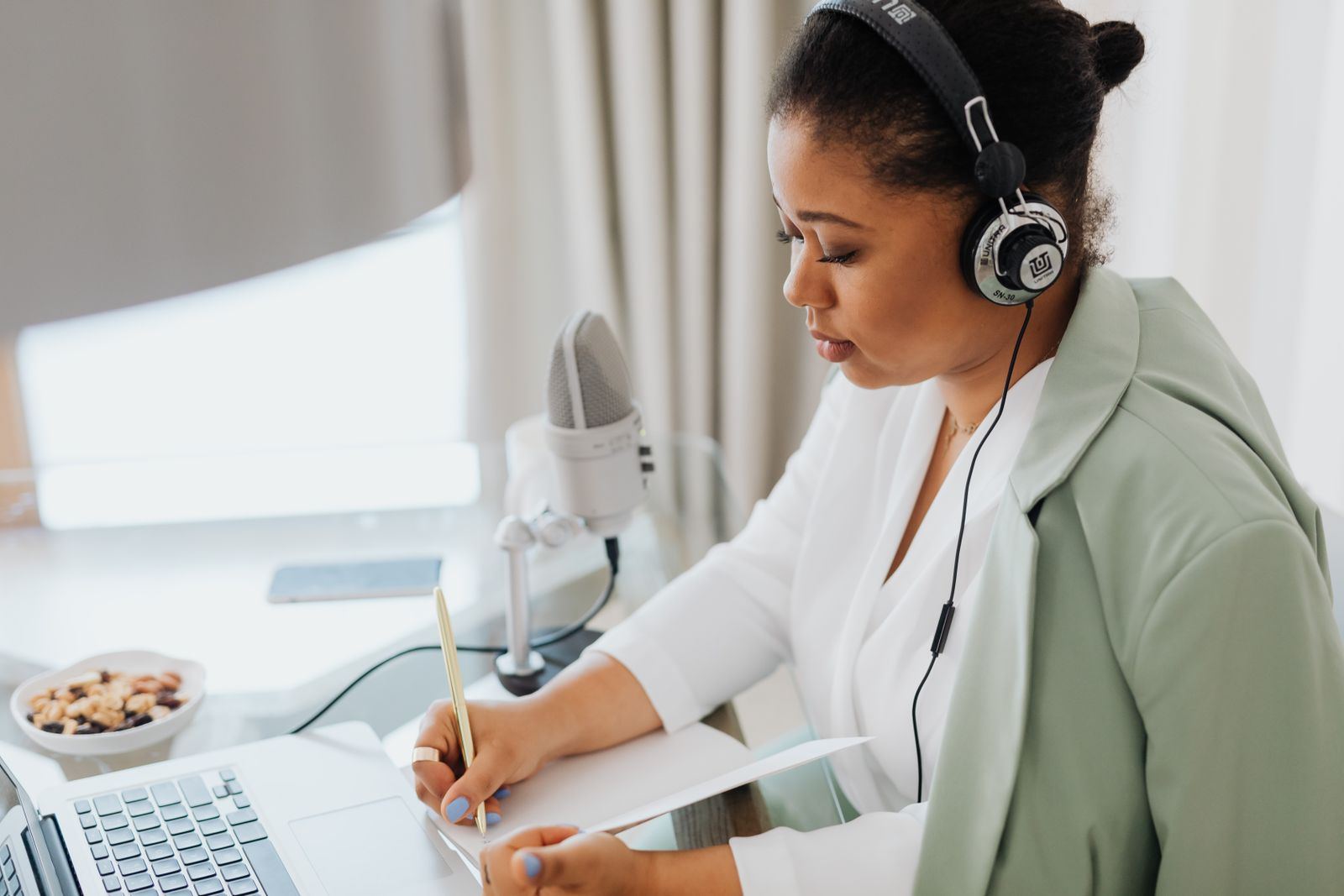 Woman wearing headphones taking notes beside a laptop